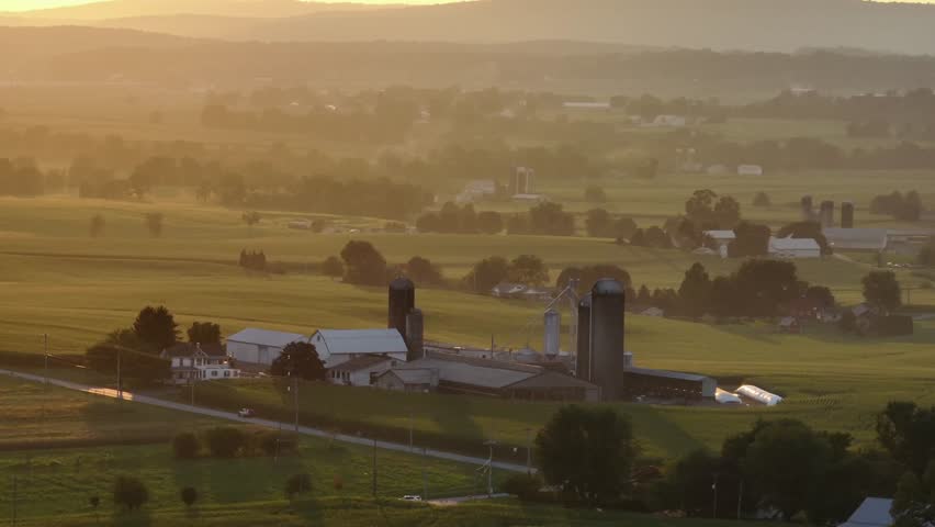 Peaceful and quaint scenic landscape with rusty traditional farmsteads at sunrise. Aerial orbit wide shot. Rural suburbia in American town. Silo storage and Barns in ephrata, Pennsylvania.