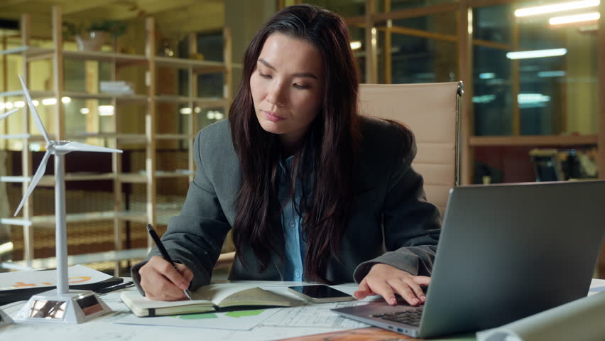 Asian business woman architect thinking green energy windmill electric power plan businesswoman engineer small wind turbine on table electricity clean ecology company Chinese Japanese girl thoughtful