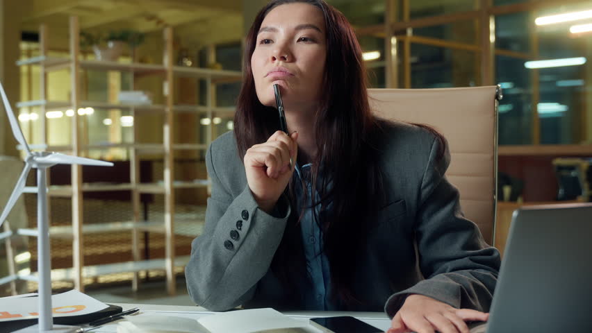 Asian business woman architect thinking green energy windmill electric power plan businesswoman engineer small wind turbine on table electricity clean ecology company Chinese Japanese girl thoughtful