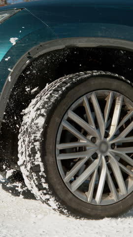 SLOW MOTION, LOW ANGLE, CLOSE UP, DOF: Fresh snow flies up from a large SUV's spinning wheel. Car's wheels spin in place and spew up pieces of snow as it attempts to gain traction on the slippery road
