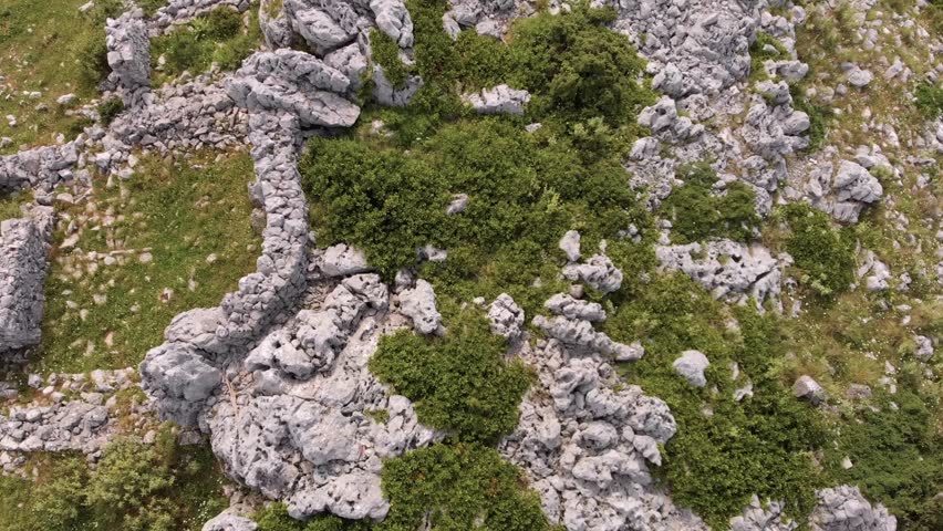 An aerial view reveals ancient stone structures and walls nestled within a rugged, rocky landscape on Corfu Island, Greece.