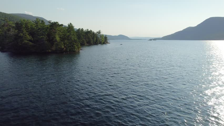 A slow forward-moving drone shot, flying over the shoreline of Floating Battery Island on Lake George, New York, in the Adirondack Mountains in September.