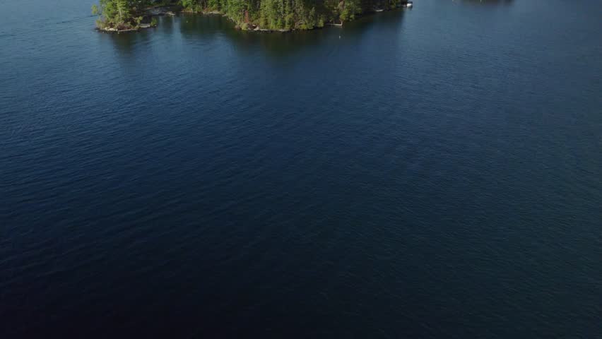 A slow forward-moving panning up drone shot, revealing Floating Battery Island on Lake George, New York, in the Adirondack Mountains in September.
