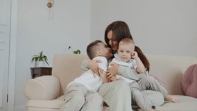 Mother sits on a sofa embracing her seven and two year old sons, all smiling and enjoying tender family closeness. Warm emotions, parenting love, and bonding time at home. High quality 4k footage - Powered by Shutterstock - Get 15% off with code: PIKWIZARD15