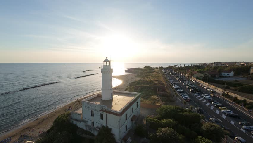 Sunset view of lighthouse by the shoreline with highway and beach
