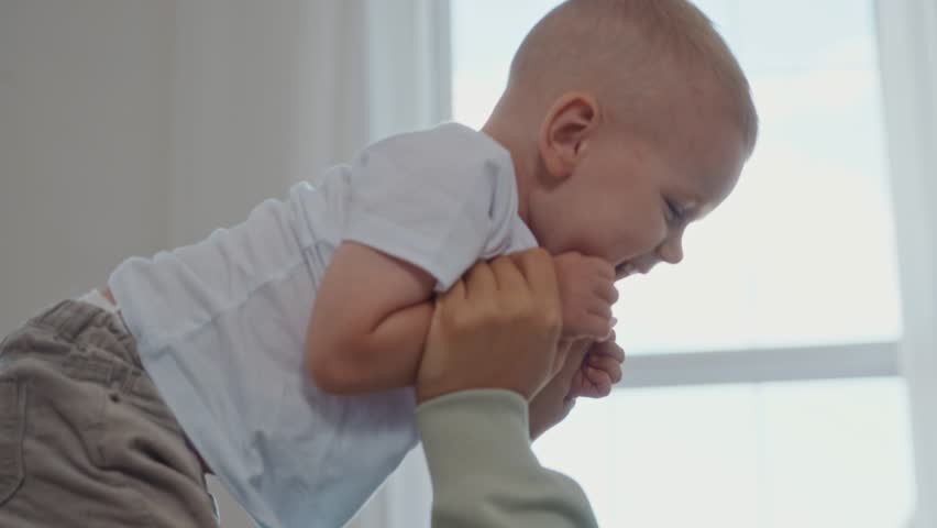Close up of smiling toddler being lifted high by his mother as they laugh and play together in a bright room. A joyful parenting moment full of love and emotional bonding. High quality 4k footage