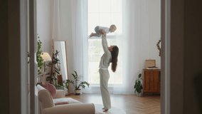 Smiling mother lifts her two year old toddler high into the air while playing together in a bright living room. Joyful parenting, laughter, and tender family bonding moment. High quality 4k footage - Powered by Shutterstock - Get 15% off with code: PIKWIZARD15