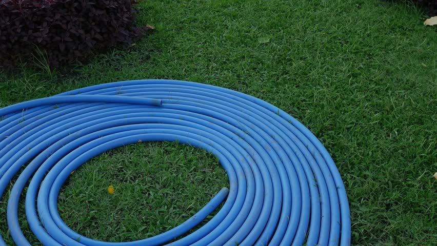 Blue Water Hose Coiled in Spiral Pattern on Green Grass Lawn - Garden Equipment and Yard Work.