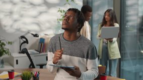 Pensive thinking African American informal business man businessman male guy startup owner writing notes in office on background of multiracial colleagues working with laptop talking multiracial team - Powered by Shutterstock - Get 15% off with code: PIKWIZARD15