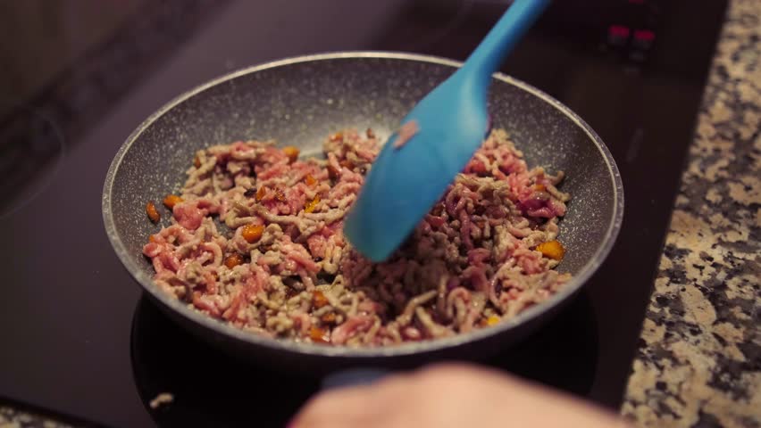 Mince meat with chopped carrots cooking on frying pan on induction stove. Cooking delicious dish with fresh mince meat and vegetables at home.