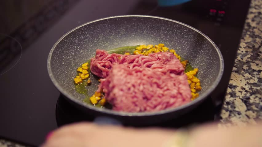 Mince meat with chopped carrots cooking on frying pan on induction stove. Cooking delicious dish with fresh mince meat and vegetables at home.