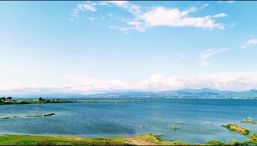The video shows the edge of Mangla Dam,a bare mud in the water, behind it the mountains of Kashmir, and the blue sky and water. It is a very captivating scene