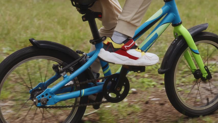 Detail shot shows childs legs pedaling bike along forest trail, symbolizing motion, health, and digital detox in nature. High quality 4k footage