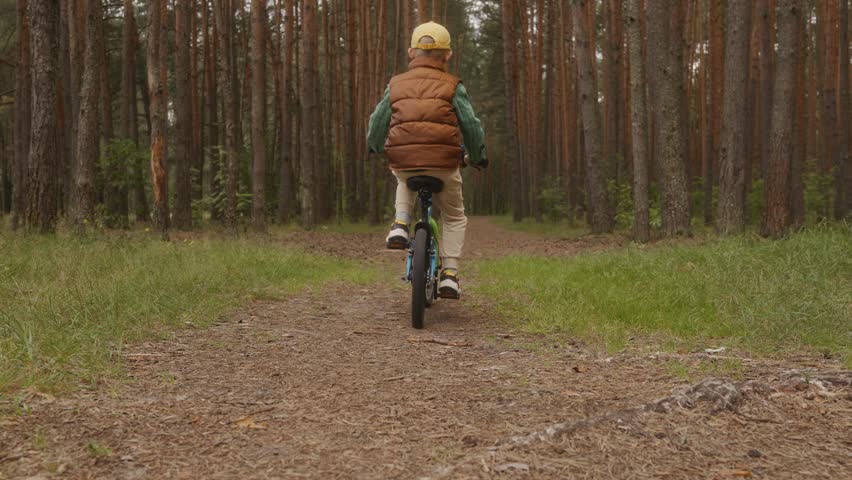 Seven-year-old boy rides his bike deeper into the forest, enjoying nature without gadgets. Simple childhood activity illustrates digital detox and outdoor freedom. High quality 4k footage