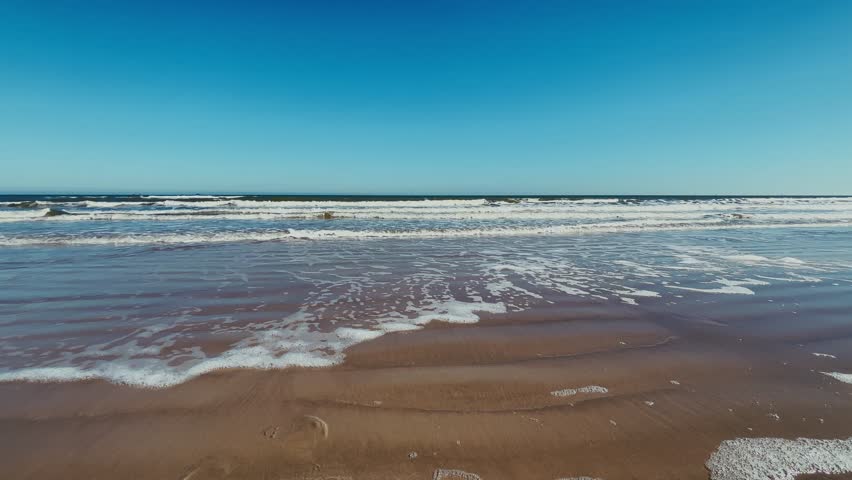 Waves wash over sandy shore at Daytona Beach Florida under clear blue sky