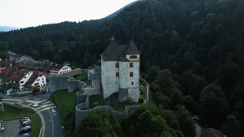 Aerial view of Valangin Castle surrounded by a lush forest and a quaint town featuring buildings with terracotta roofs, Neuchâtel, Switzerland.