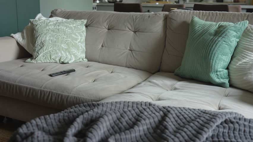 Woman in striped sweater holds remote control while seated on a beige couch