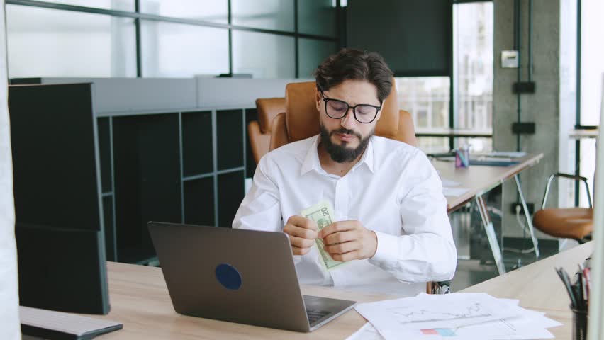 Man counting cash while working at a modern office desk in a bright workspace during daytime hours