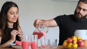 Middle Eastern couple making watermelon smoothie at home. Bearded attractive man pours fresh smoothie from blender into glasses on the table, woman watches. Healthy drink from ripe watermelon. - Powered by Shutterstock - Get 15% off with code: PIKWIZARD15