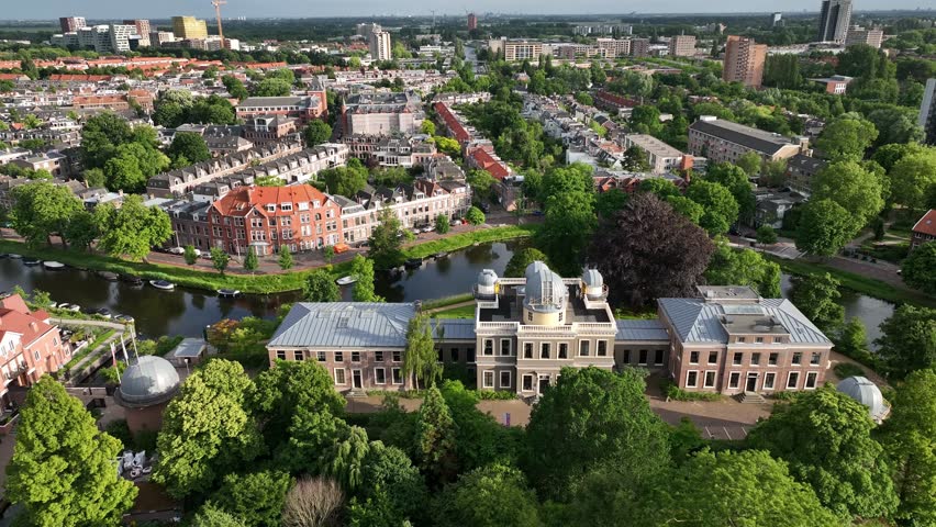 Aerial descending view of Leiden Observatory and nearby canal in Leiden, Netherlands, framed by summer greenery.
