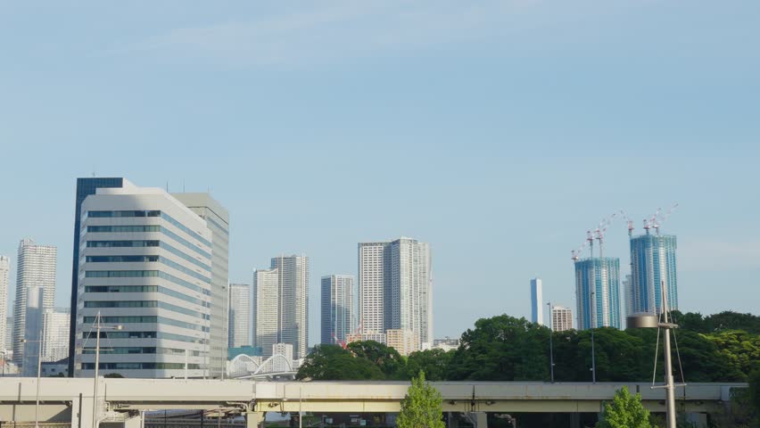 A view of a modern Tokyo skyline with multiple high-rise buildings, including two under construction with cranes.