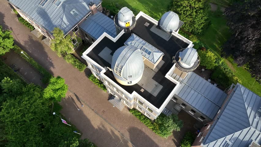 Aerial zoom in focusing on the historic Leiden Observatory domes and architectural details surrounded by trees in Leiden, Netherlands.