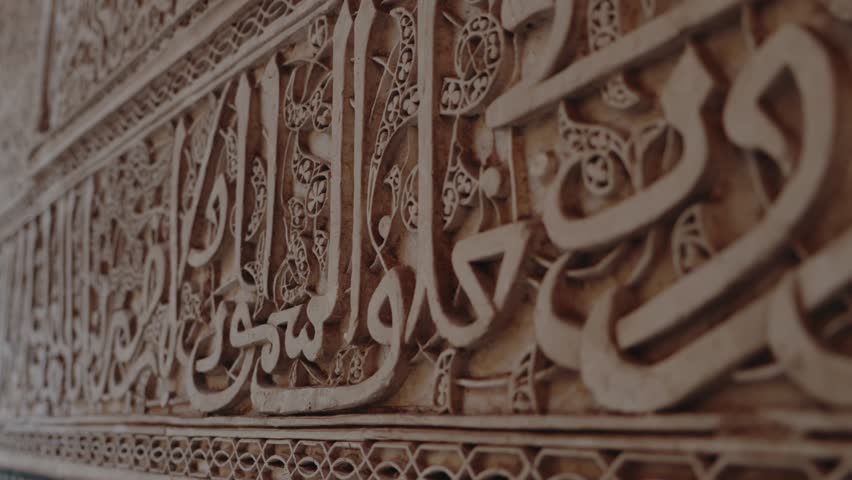 Close-up of intricate Islamic calligraphy carved into a wall. The ornate design showcases the rich artistic heritage of Moroccan architecture. Intricate Islamic Calligraphy Carved
