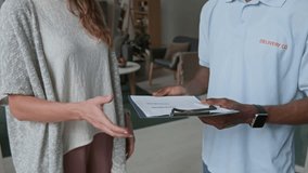 Close up of unrecognizable African American courier in pastel blue t-shirt with sign label saying delivery co giving form to woman to sign it - Powered by Shutterstock - Get 15% off with code: PIKWIZARD15