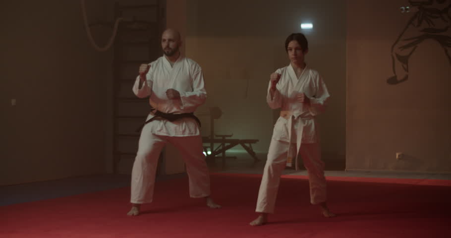 Father and son in kimonos train kicks in martial arts gym