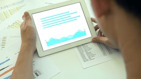 A person interacts with a tablet displaying charts and reports, surrounded by printed data sheets. This image captures the essence of data analysis and technology in a modern workspace. - Powered by Shutterstock - Get 15% off with code: PIKWIZARD15