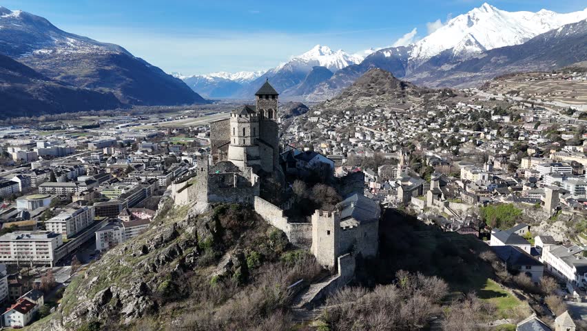 Drone video of Sion old town and fly by the castle "Chateau La Valère" with the snow caped Alps in the background, Valais Switzerland