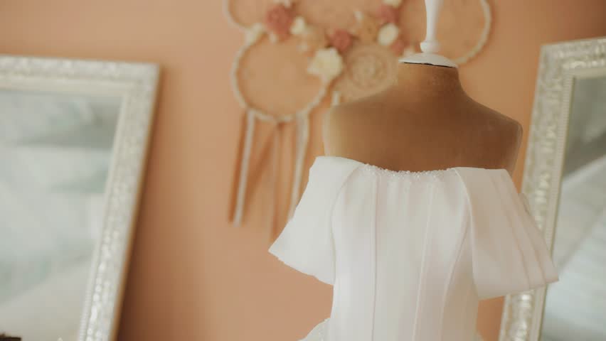 A white wedding dress is hanging on a mannequin hanger in the bride's room.
