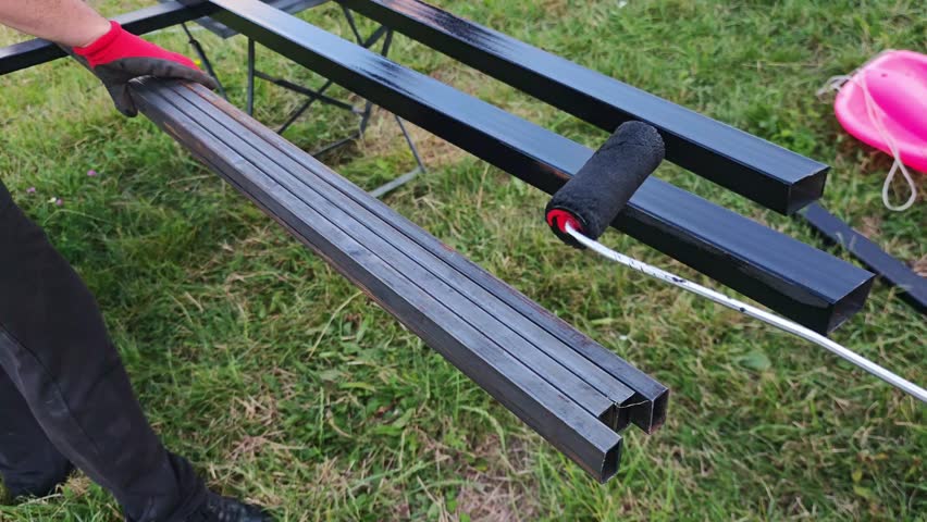 Construction professional carefully painting black coating onto metal bars with precision, applying roller during outdoor renovation project