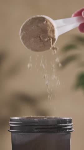 protein powder spills in cup from measure scoop.  whey sports nutrition. dry mixture for preparation of sporting or dietary drink.