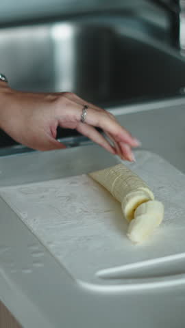 Female cutting banana near sliced red apples on wooden cutting board