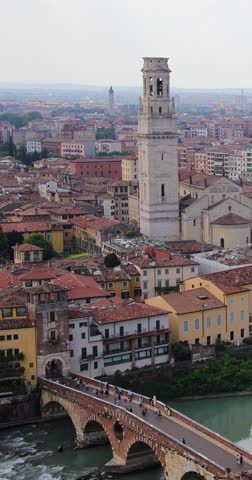 Portrait vertical footage of the beautiful city of Verona in Italy showing the town centre along side the river Adige with a bridge going over the water in the summer time on a sunny day