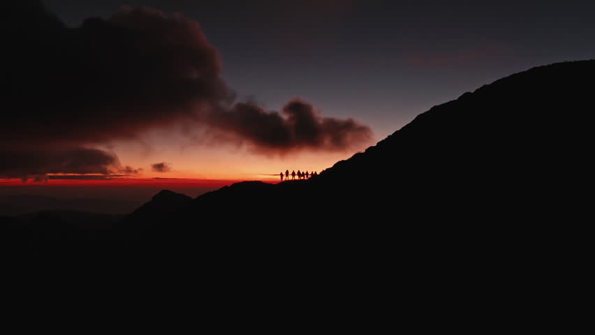 A stunning aerial view captures a vibrant sunset behind towering mountains