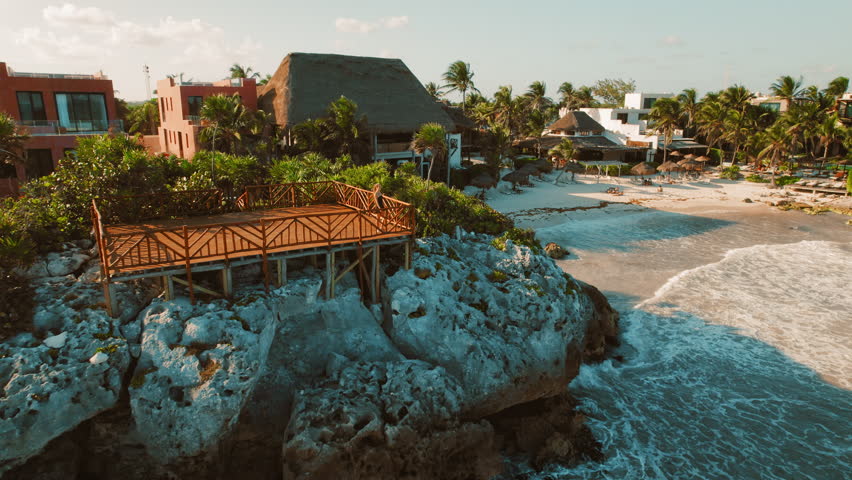 Woman on a wooden deck overlooking tropical resort scenic beach town with cliffside lookout and palm trees facing turquoise sea in Tulum, Mexico