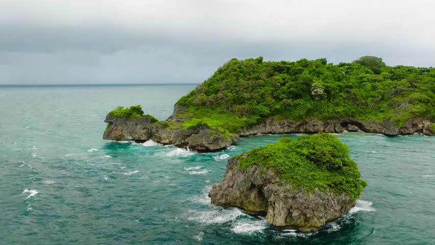 A tiny green islet surrounded by vibrant turquoise waters with visible waves and marine life below the surface. Boracay Island, Philippines.