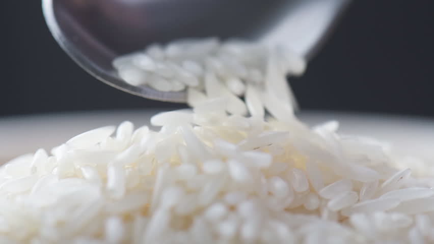 Cereal grains of Jasmine rice are pouring out of a spoon. Macro shot. Closeup view of long-grain variety of fragrant rice. Healthy eco food. Product of organic farming.