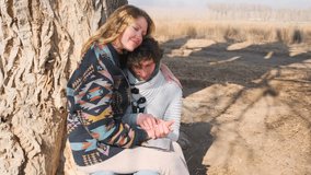 Nestled at the base of a tree in an autumn park, a couple shares a tender moment. The woman leans into her boyfriend with a smile, squeezing his hand as he leans in, feeling the strength of their bond - Powered by Shutterstock - Get 15% off with code: PIKWIZARD15