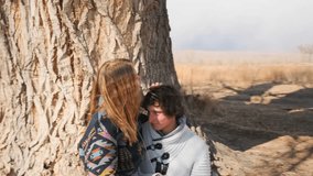 A young couple shares a romantic moment at the base of a large tree. The man sits leaning against the trunk as the woman gently strokes his hair, gazing at him with warmth and love. - Powered by Shutterstock - Get 15% off with code: PIKWIZARD15