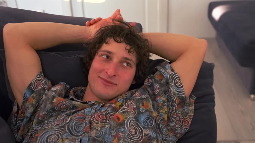 Smiling, the man draws his girlfriend toward him over the back of the couch. The couple laugh and fall into a romantic embrace, feeling the warmth and deep connection between them.