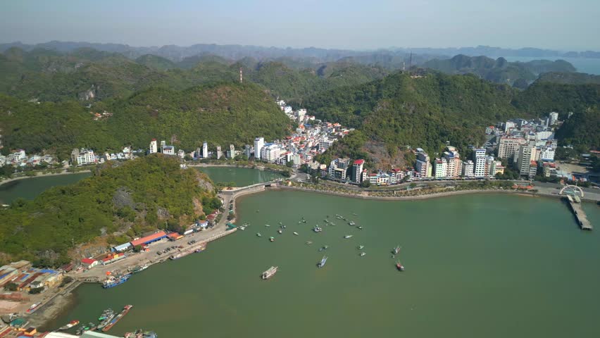 Drone aerial view of Cat Ba town in Vietnam with harbor, coastline, and limestone hills. Scenic urban landscape by the sea, surrounded by mountains and gateway to Lan Ha Bay and Ha Long Bay.