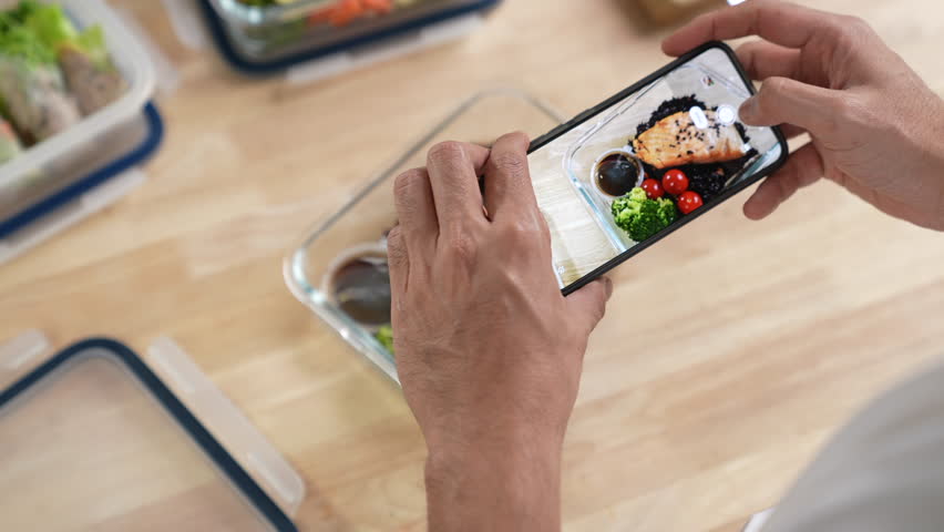Man taking photo with mobile phone while preparing healthy homemade meal prep with fresh food at home.
