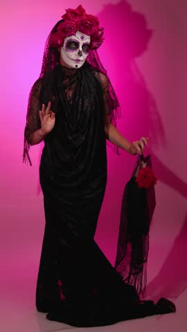 Woman in complete Calavera Catalina attire. She is wearing sugar skull makeup and holding a rose in observance of the Day of the Dead tradition.