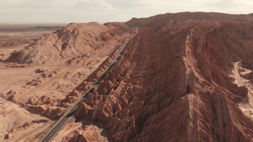 Aerial drone shot of a winding road cutting through dramatic rock formations in the heart of the Atacama Desert Chile during a golden summer sunset with deep shadows and rich earthy tones