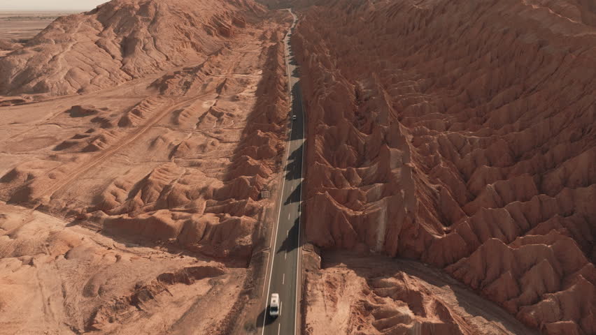 Aerial drone shot of a winding road cutting through dramatic rock formations in the heart of the Atacama Desert Chile during a golden summer sunset with deep shadows and rich earthy tones