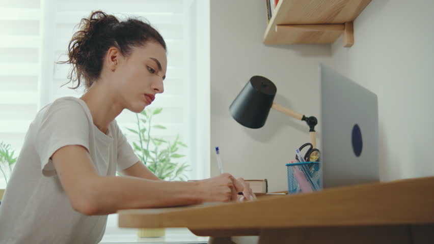 Focused woman writing notes at a desk with a laptop in a bright and modern room during daytime