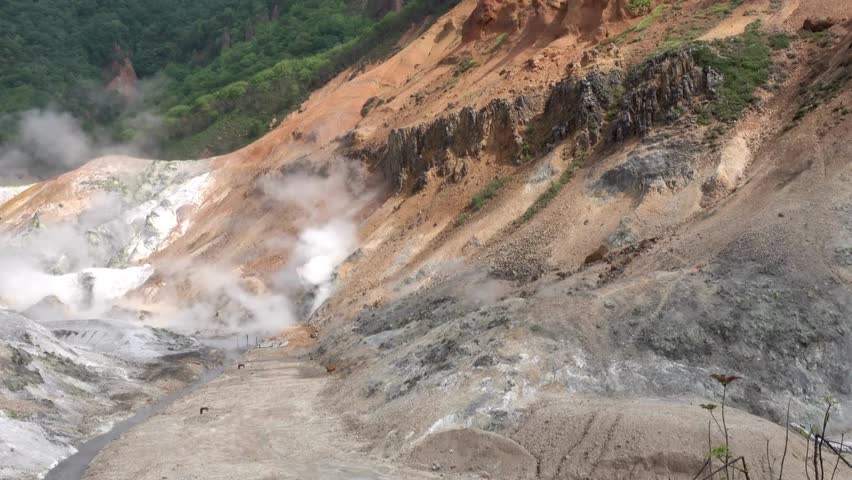 Steam rises from vents in a barren geothermal valley, showcasing colorful, mineral rich cliffs and the raw, powerful forces of volcanic activity.